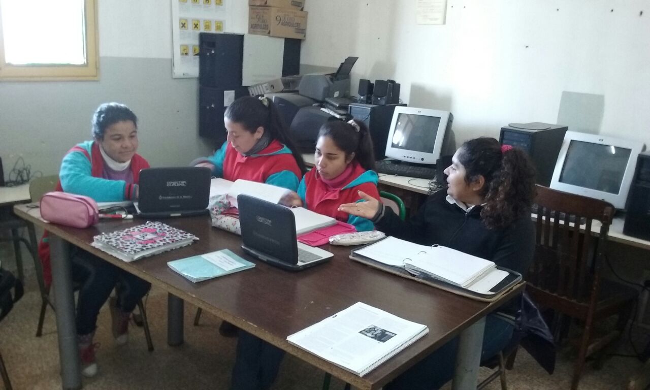 Estudiantes trabajando con cuadernos y computadoras portátiles en un aula.